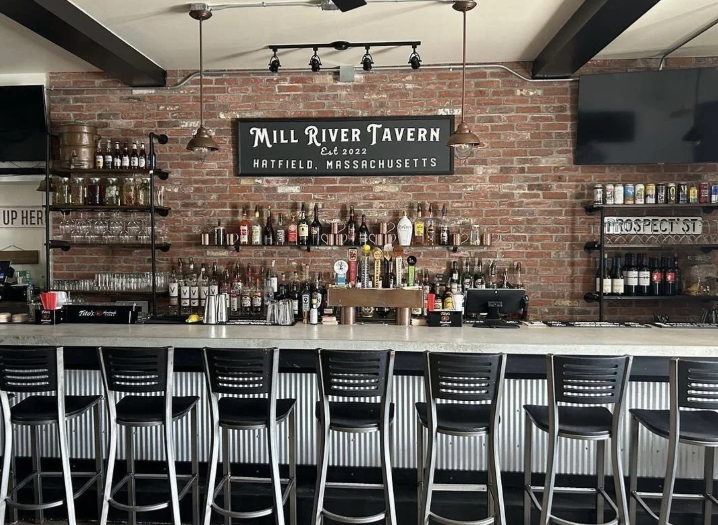 Mill River Tavern bar with stools, exposed brick, and full bottle display