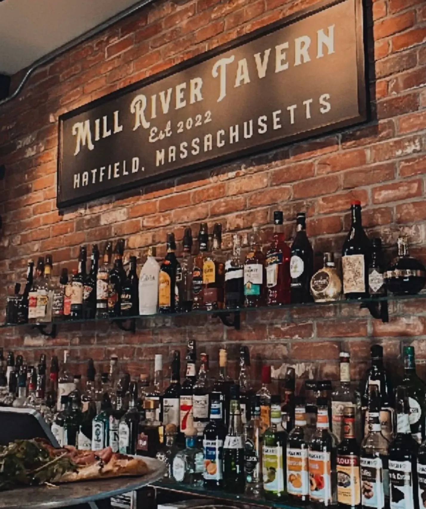 Mill River Tavern sign mounted on exposed brick above the bar